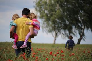 man carrying to girls on field of red petaled flower by Juliane Liebermann courtesy of Unsplash.