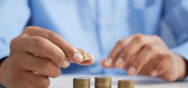 a person stacking coins on top of a table by Towfiqu barbhuiya courtesy of Unsplash.